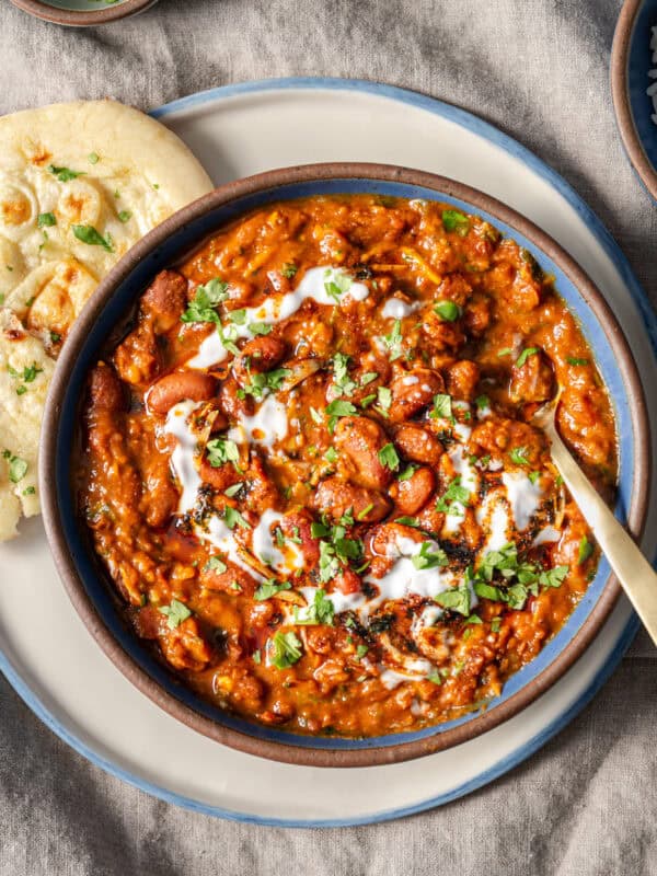 bowl of rajma masala topped with yogurt and cilantro sitting on a plate with a piece of naan.