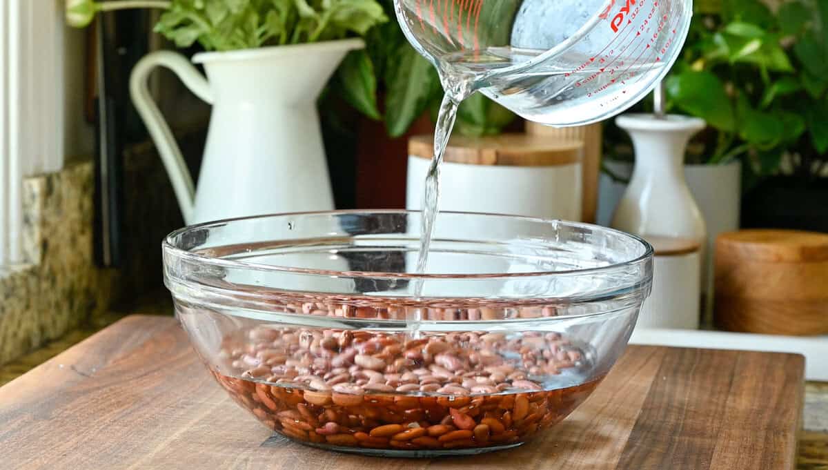 person pouring water over dried kidney beans in a large glass bowl.