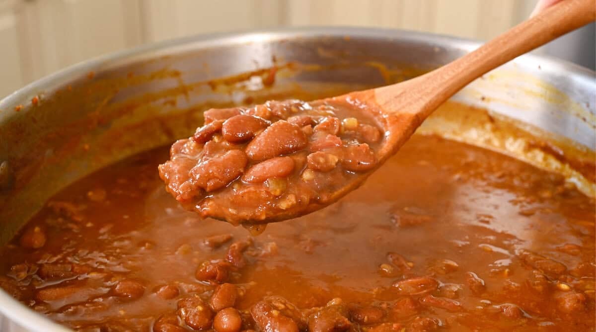 person holding a cooking spoon with rajma masala over the pan.