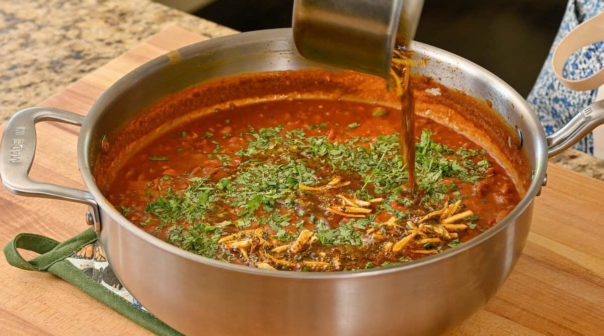 person pouring the tadka over the rajma masala.
