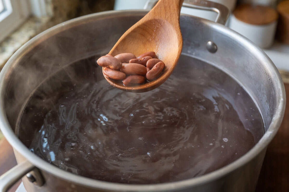 spoon adding cooked beans to a large pot of water.