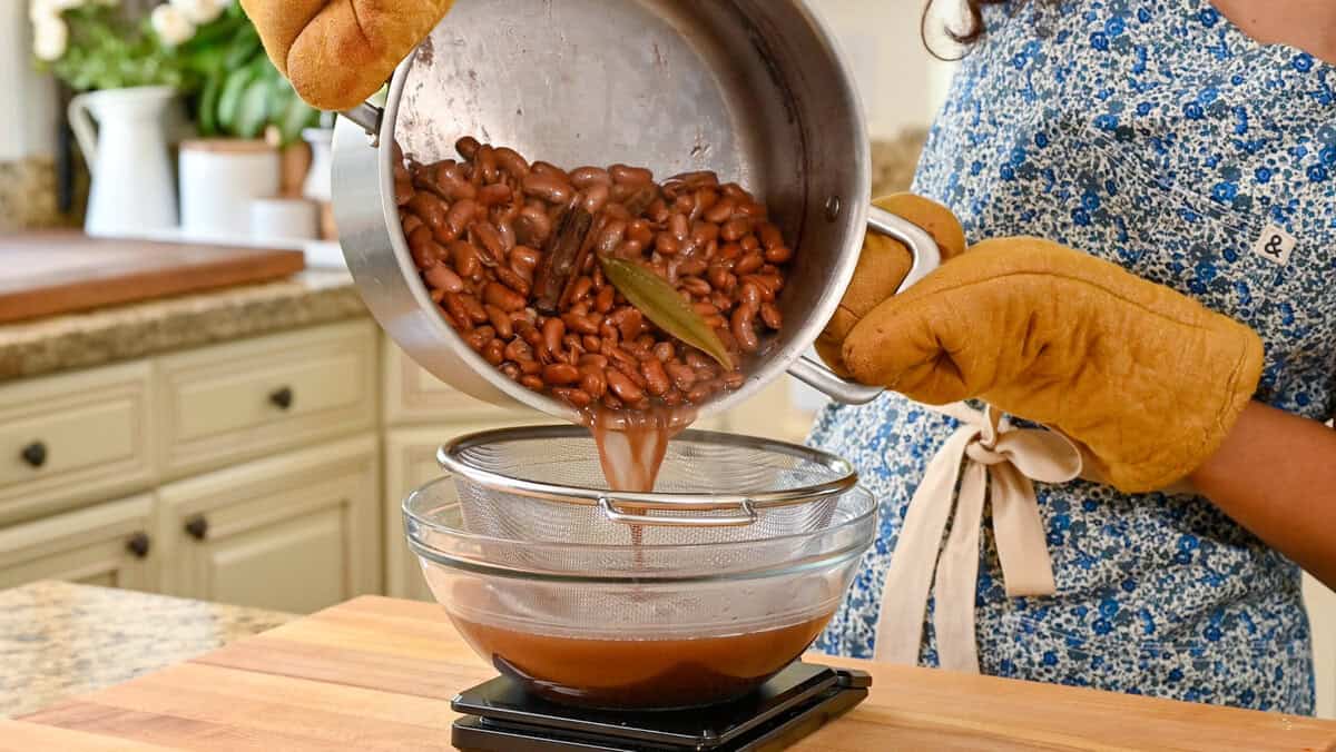 person straining beans from cooking liquid with a colander fitted inside a glass bowl.