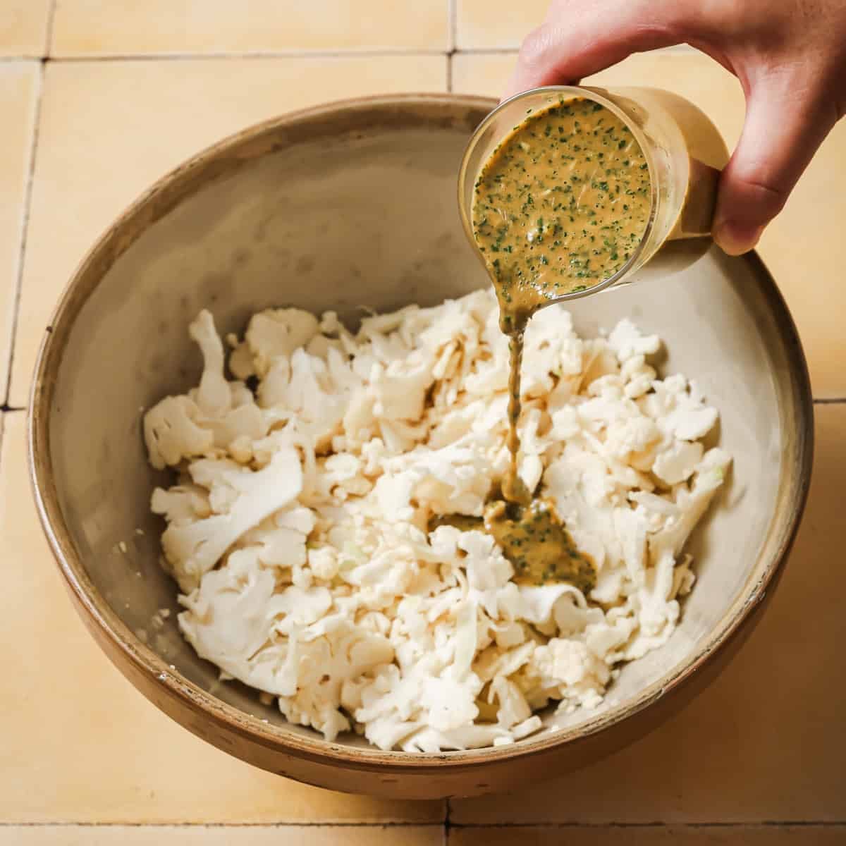 person pouring dressing over the shaved cauliflower.