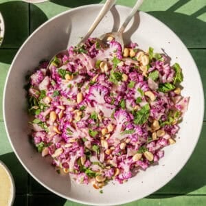 two servings spoons in a bowl of cauliflower salad on a table.