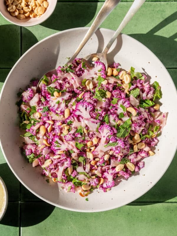 two servings spoons in a bowl of cauliflower salad on a table.