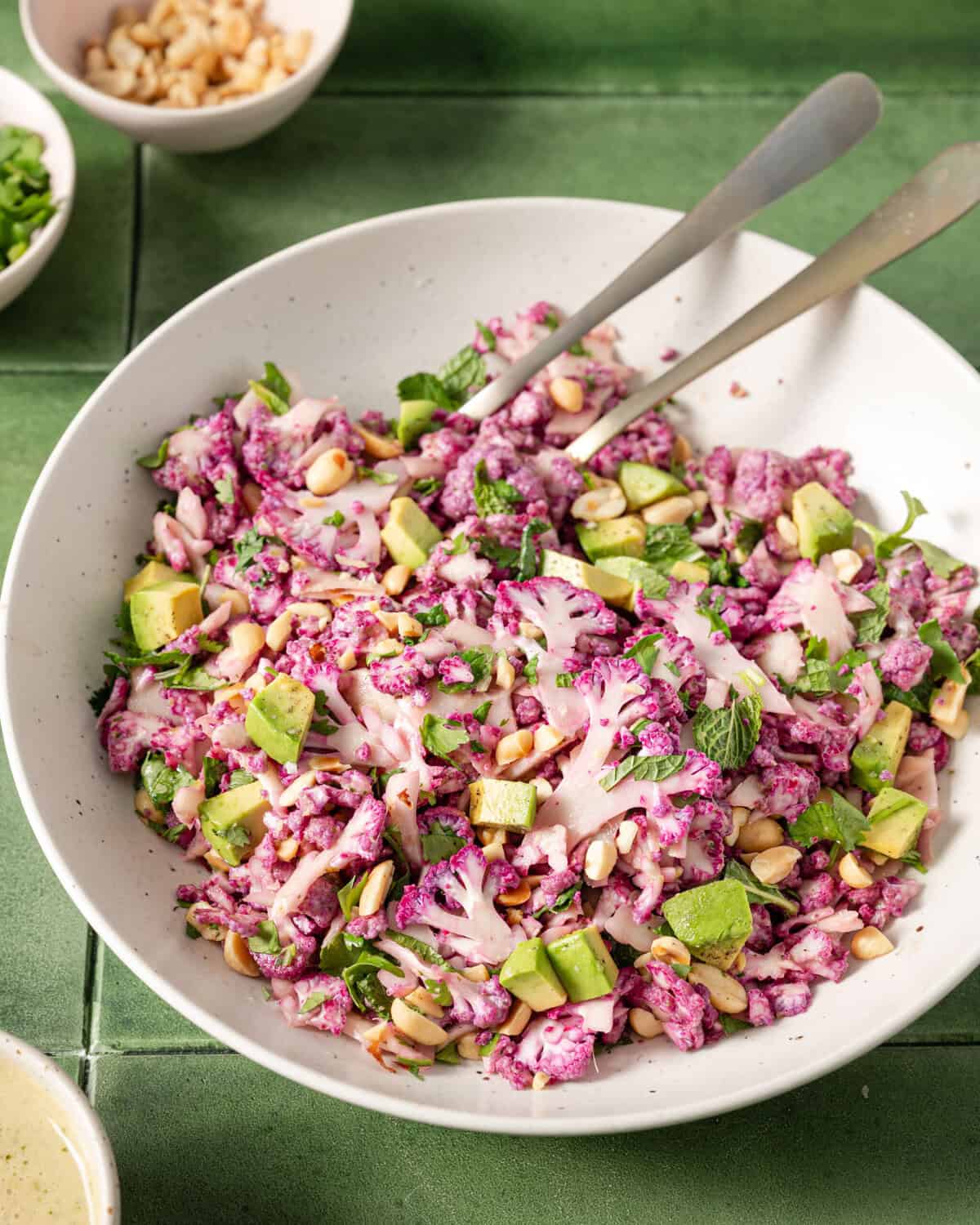 close up shot of bowl of shaved cauliflower salad with two serving spoons on a table.