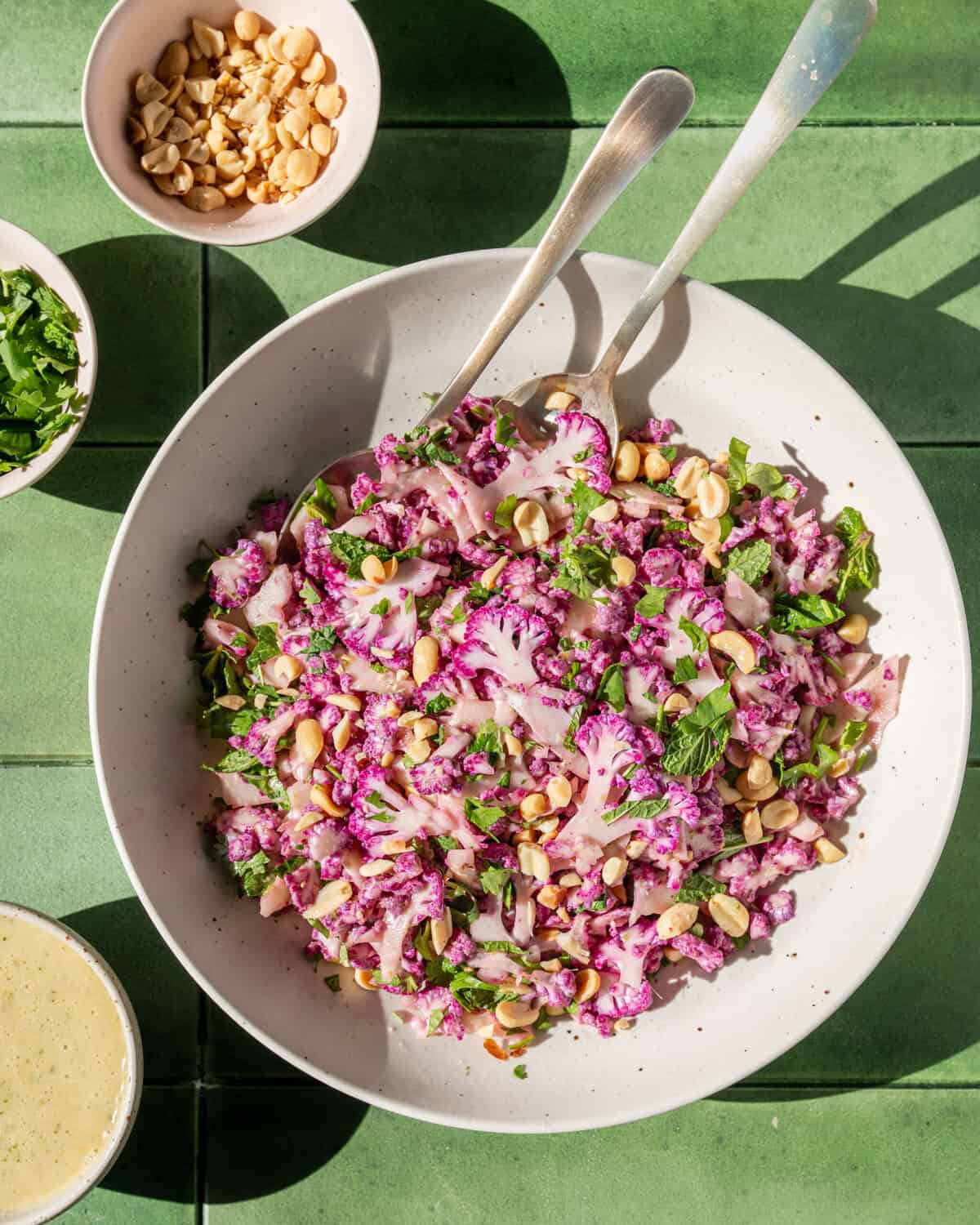 overhead view of cauliflower salad in a bowl with two serving spoons.