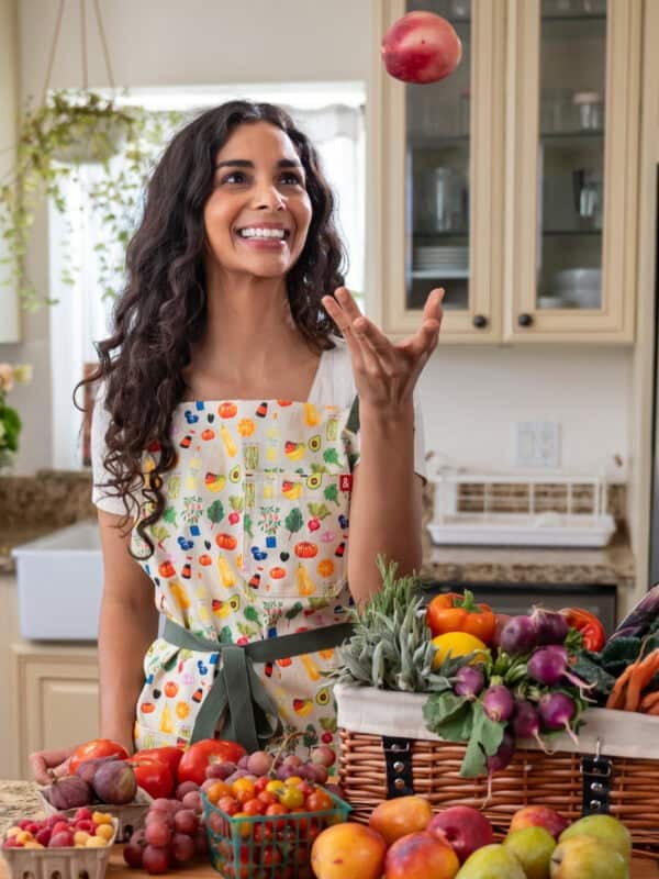 Nisha tossing fruit while custom Rainbow Plant Life apron designed with Hedley & Bennett.