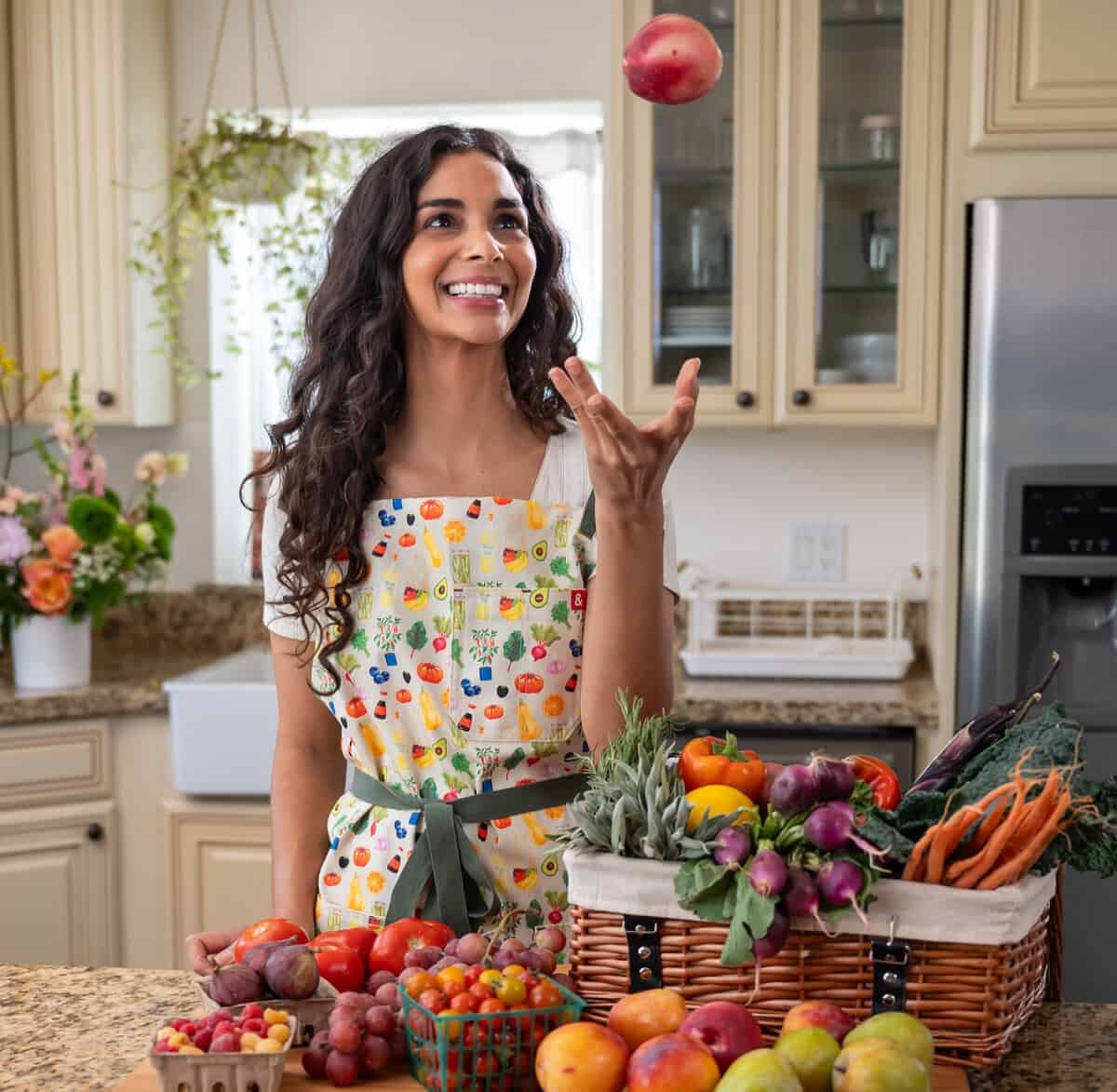 Nisha tossing fruit while custom Rainbow Plant Life apron designed with Hedley & Bennett.