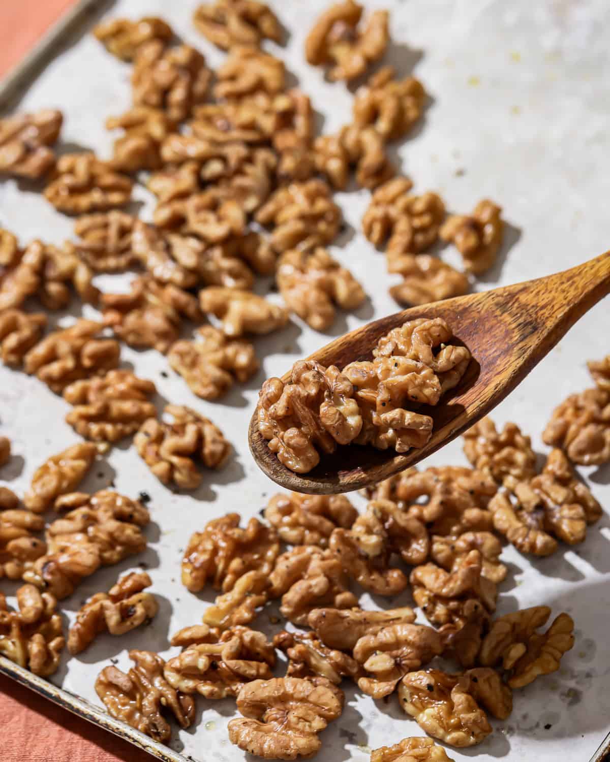 wooden spoon holding up roasted walnuts over a tray of roasted walnuts.
