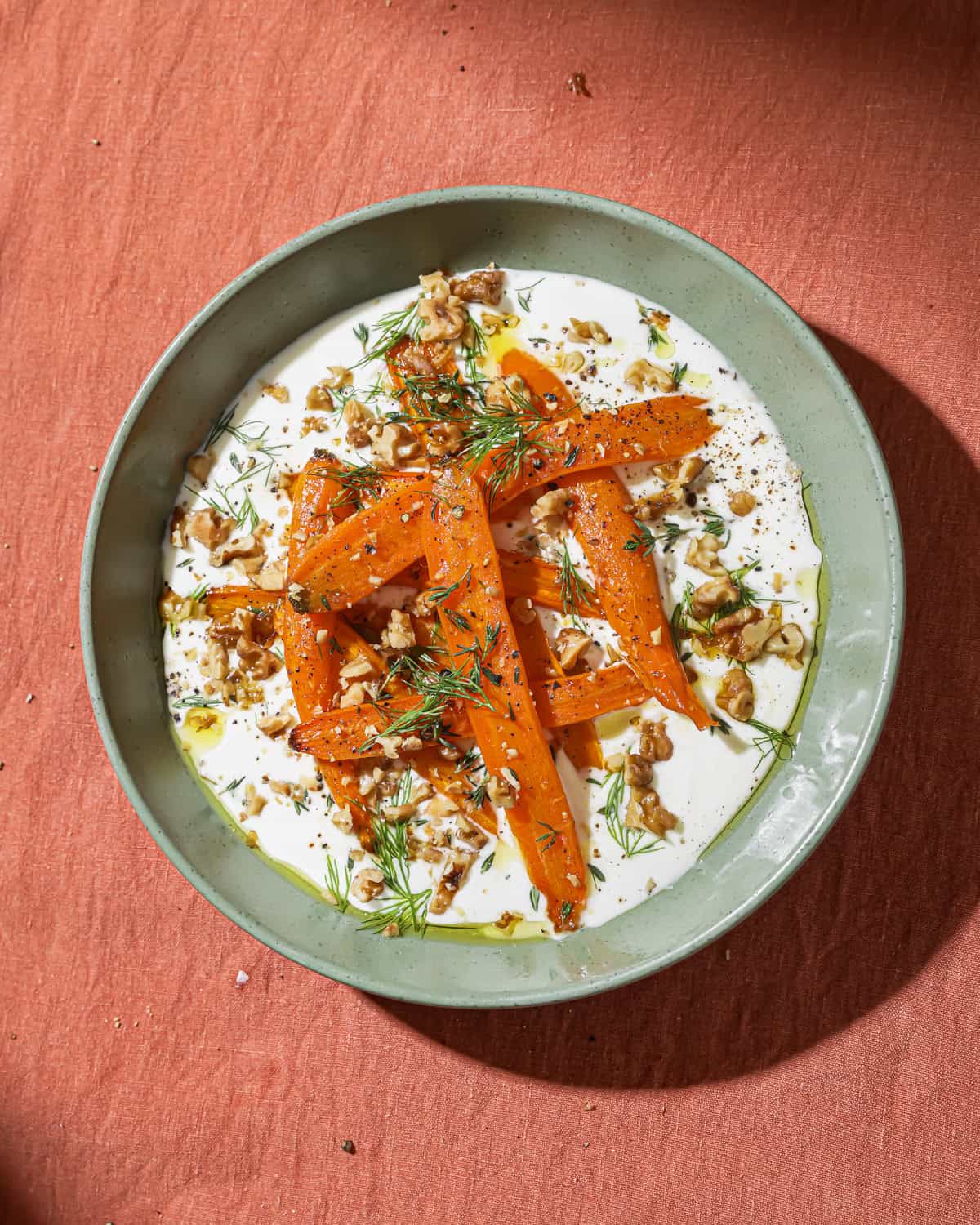 bowl of yogurt topped with marinated carrots, dill, oil and roasted walnuts.
