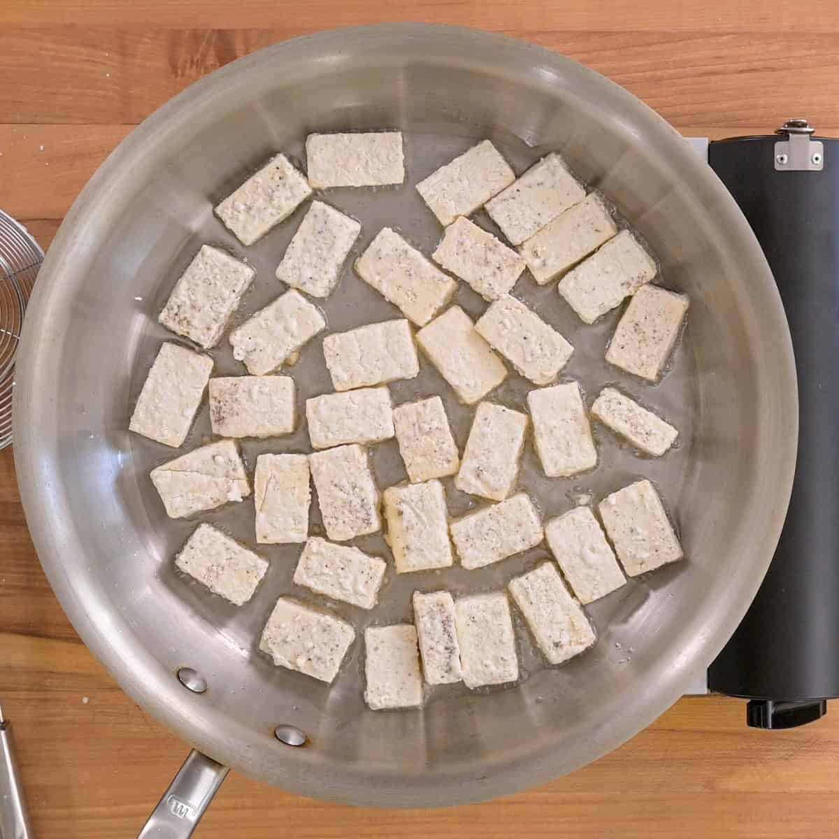Tofu pieces in a frying pan before being cooked.