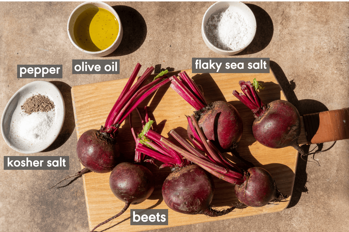 raw whole beets on a wooden cutting board next to small bowls of oil, salt and pepper on a table.
