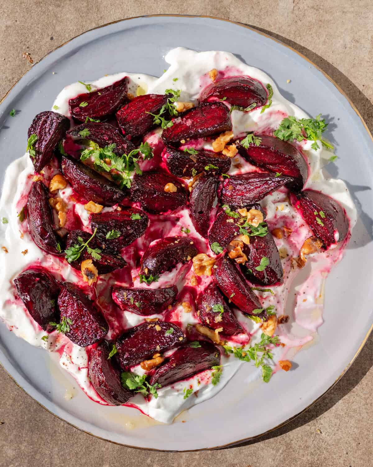 plate of yogurt topped with roasted beets, roasted walnuts and chopped parsley.