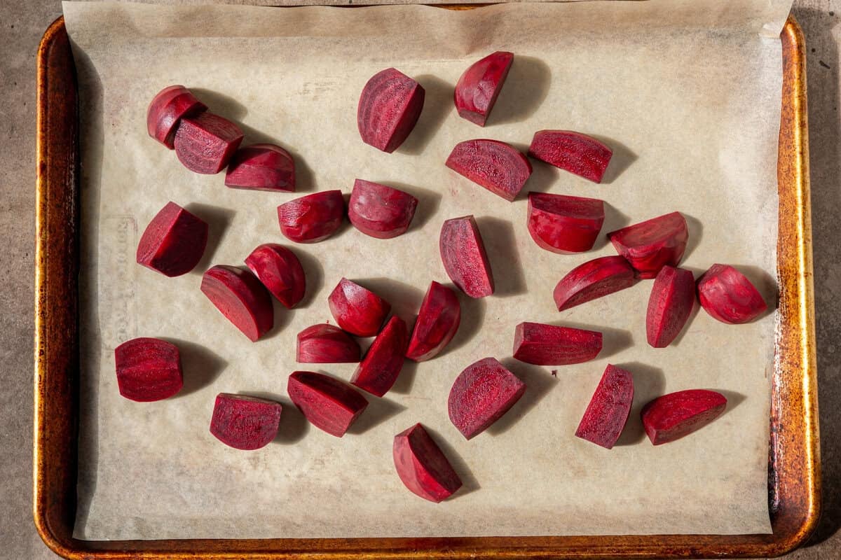 quartered beets spread out on a piece of parchment paper on a baking sheet.