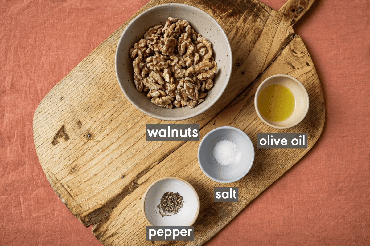 ingredients for roasted walnuts in small bowls on a wooden cutting board.