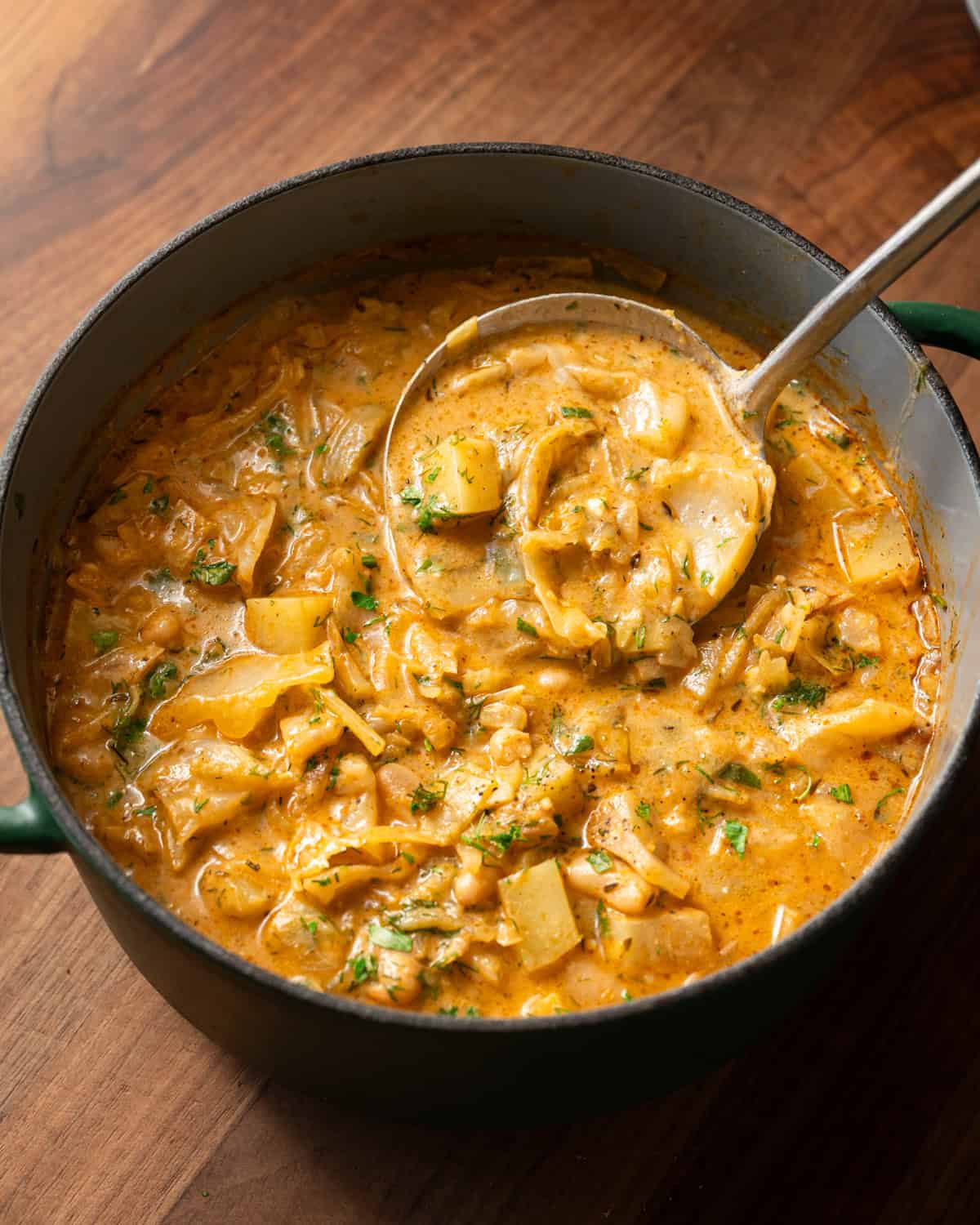 overhead shot of golden cabbage soup in pot with a ladle.