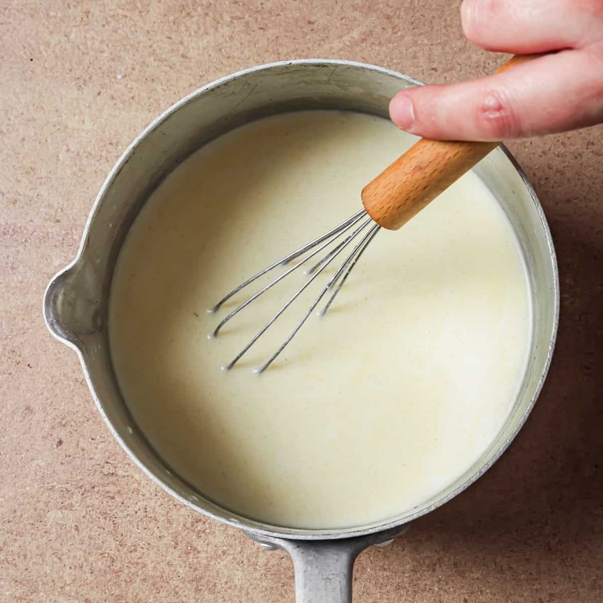 person whisking milk followed by the miso-soy sauce slurry into the roux.