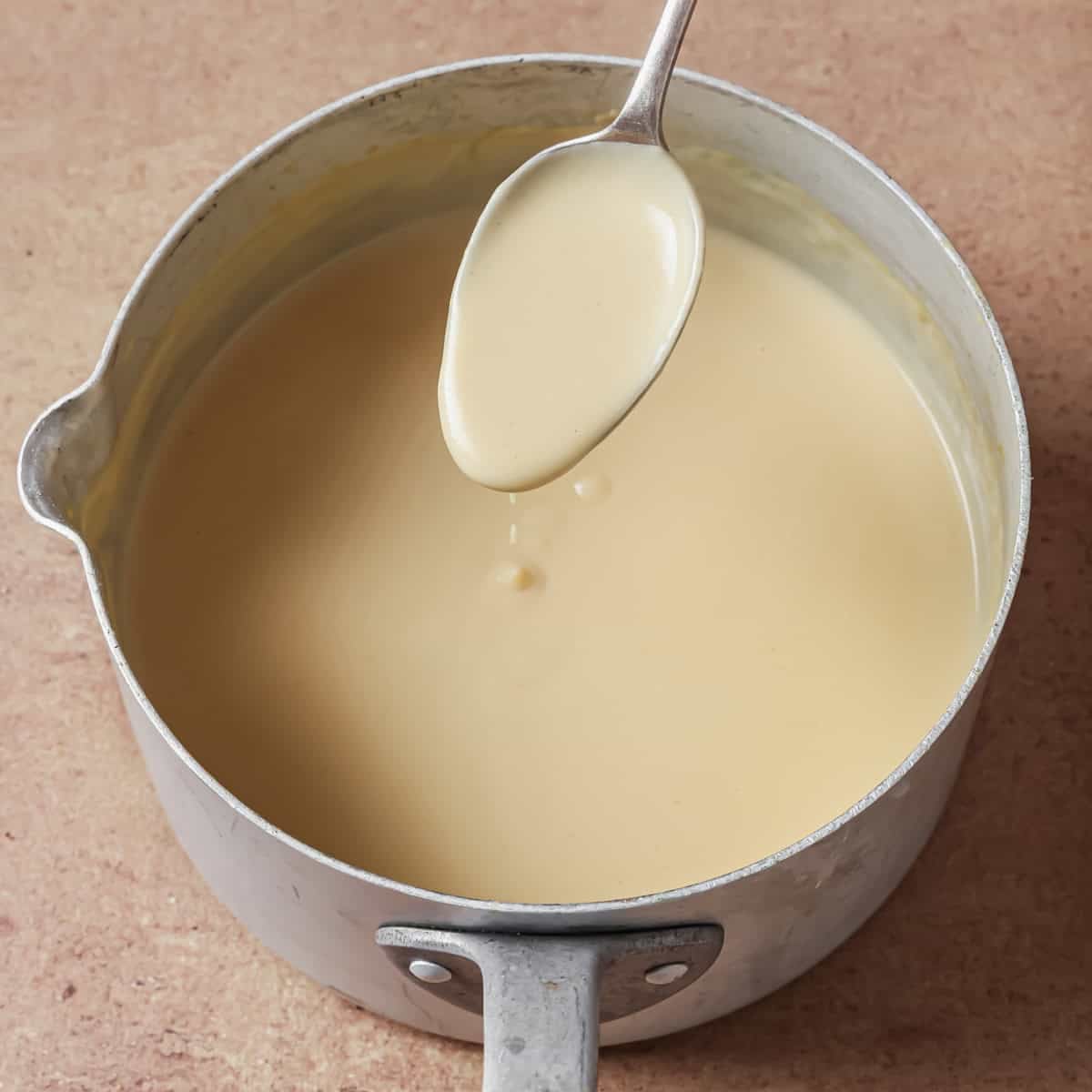 person holding a spoonful of the thickened sauce above the saucepan.