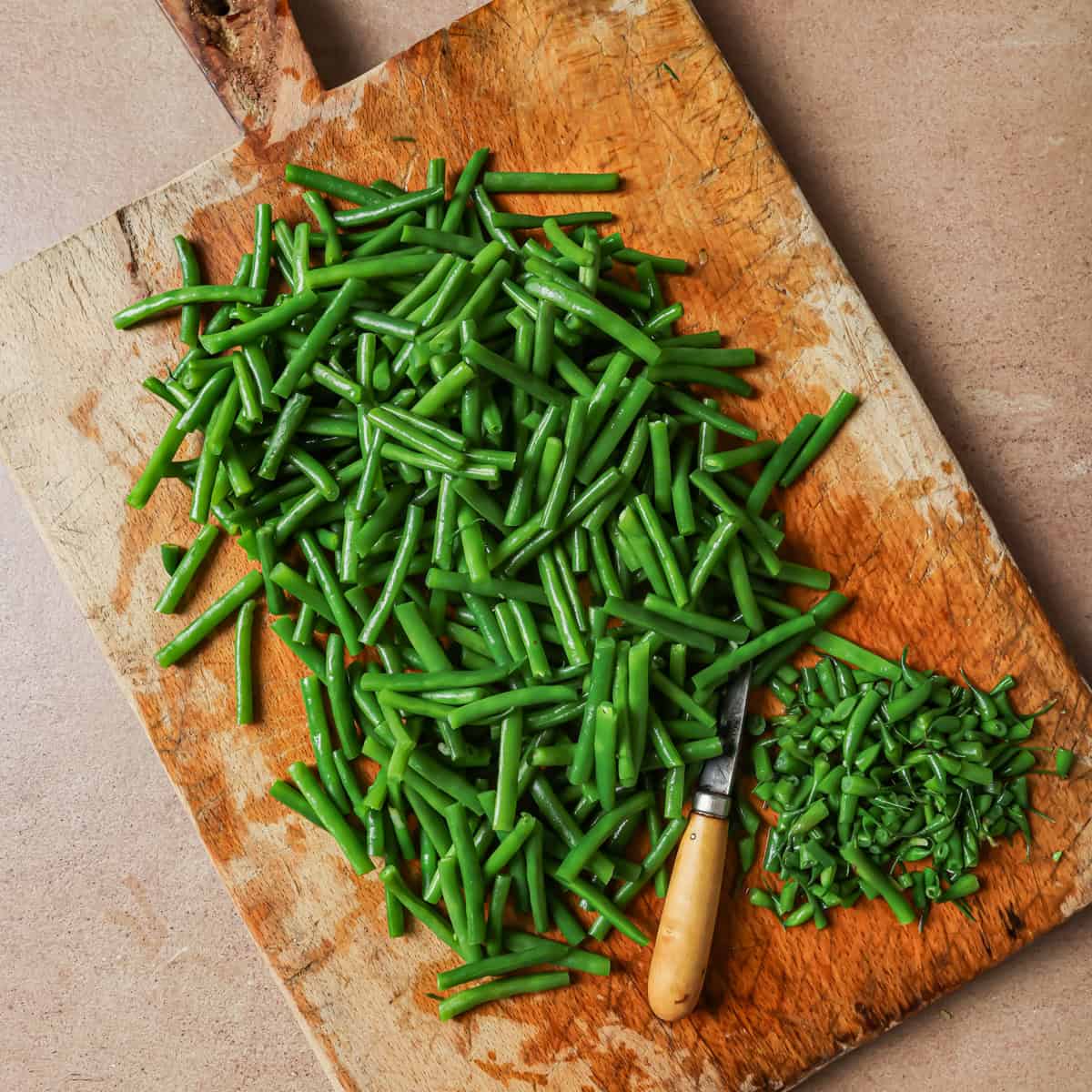 trimmed green beans on a wooden cutting board.