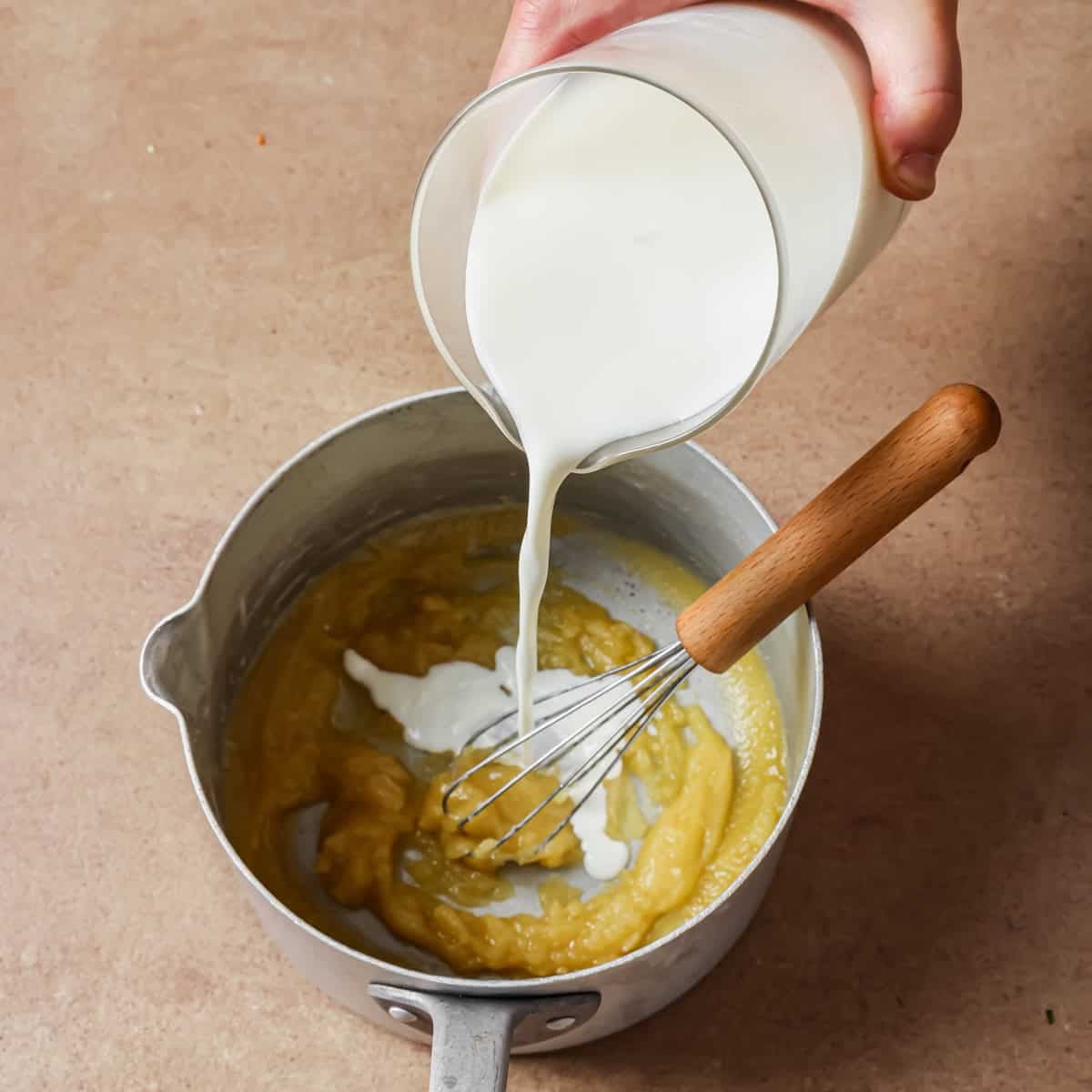 person pouring milk into butter and flour mixture in a saucepan.