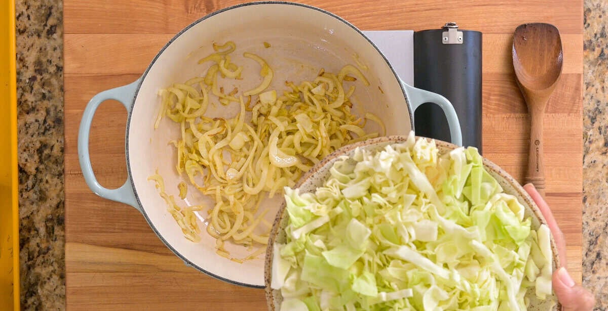 person adding cabbage, garlic and salt to the cooked fennel in the pot.